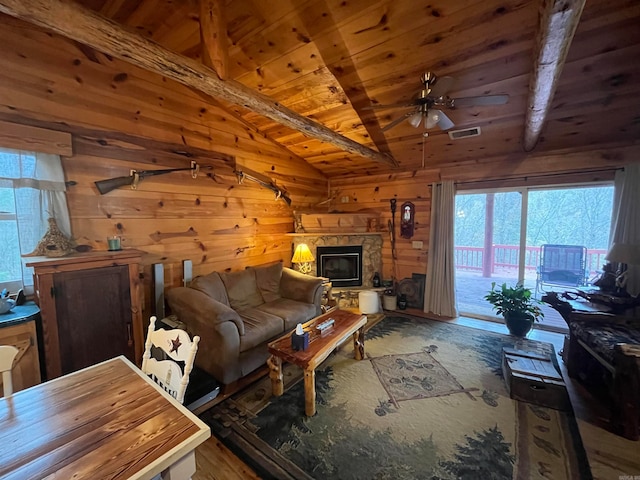 living room with wood ceiling, ceiling fan, vaulted ceiling with beams, a stone fireplace, and wood walls