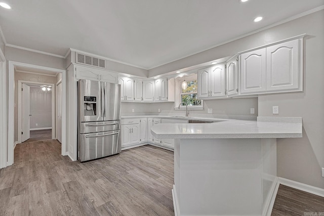 kitchen with white cabinets, sink, stainless steel fridge, ornamental molding, and kitchen peninsula