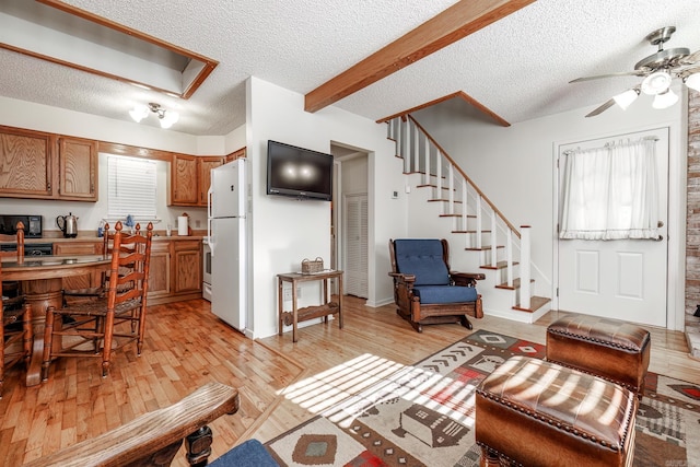 living room with ceiling fan, beamed ceiling, light hardwood / wood-style floors, and a textured ceiling