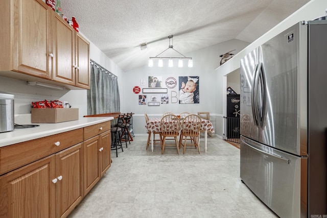 kitchen with a textured ceiling, hanging light fixtures, stainless steel refrigerator, and vaulted ceiling