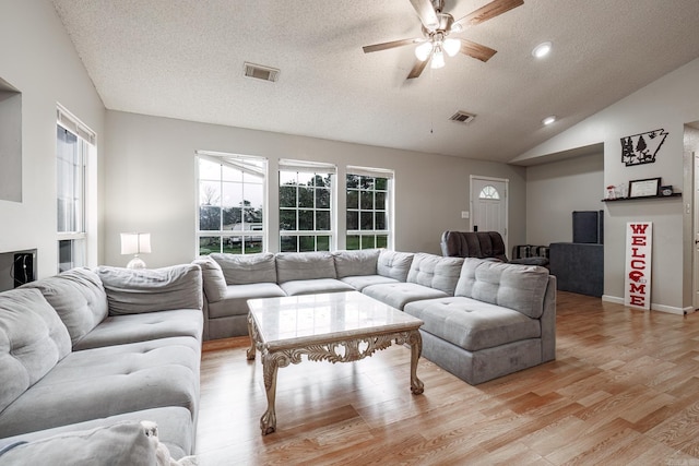 living room with ceiling fan, a textured ceiling, and light wood-type flooring