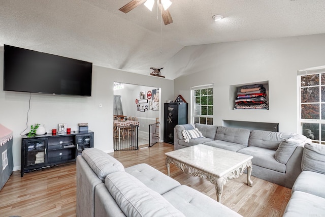 living room with a textured ceiling, ceiling fan, vaulted ceiling, and light wood-type flooring