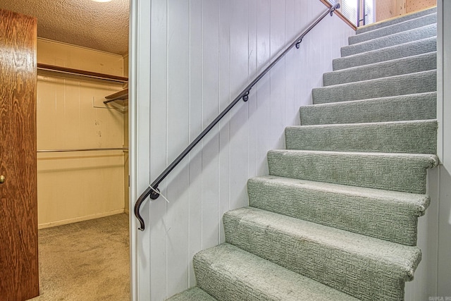 stairs featuring wood walls, carpet floors, and a textured ceiling