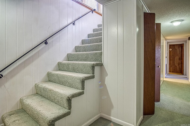 stairway featuring carpet flooring, a textured ceiling, and wood walls