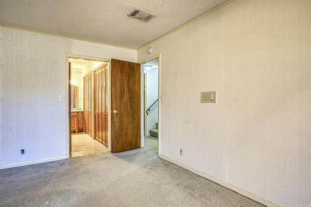 spare room featuring light colored carpet, ornamental molding, and a textured ceiling