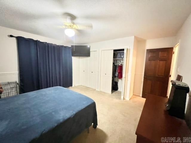 bedroom featuring a textured ceiling, ceiling fan, light carpet, and two closets