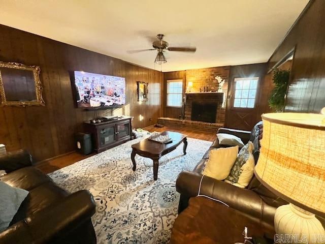 living room featuring hardwood / wood-style flooring, a brick fireplace, ceiling fan, and wooden walls