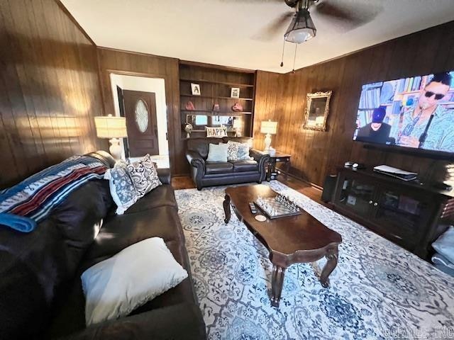 living room featuring wood walls, built in features, ceiling fan, and hardwood / wood-style flooring