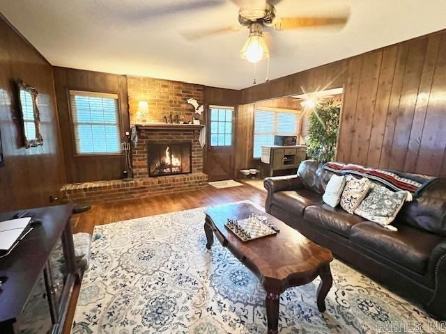 living room featuring ceiling fan, wood-type flooring, wooden walls, and a brick fireplace