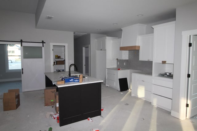 kitchen with white cabinetry, sink, a barn door, and a center island with sink