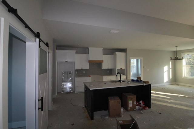 kitchen featuring white cabinetry, sink, a kitchen island with sink, a barn door, and wall chimney exhaust hood