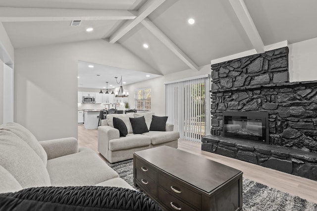 living room featuring a stone fireplace, lofted ceiling with beams, wood-type flooring, and an inviting chandelier