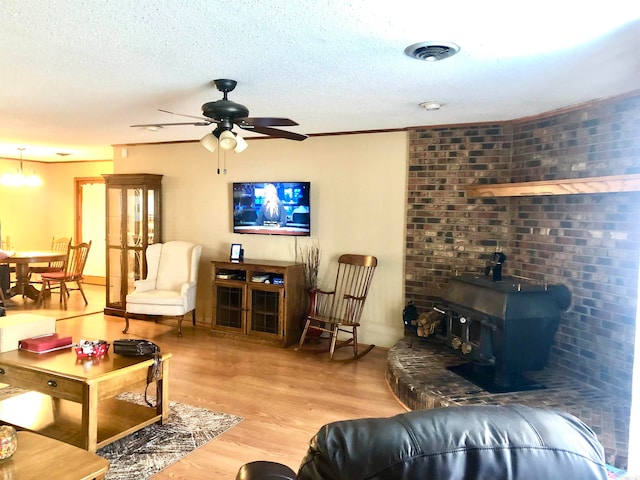 living room featuring wood-type flooring, a textured ceiling, a wood stove, and ceiling fan