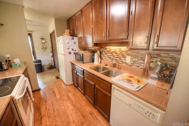 kitchen with white appliances, sink, decorative backsplash, light wood-type flooring, and a textured ceiling