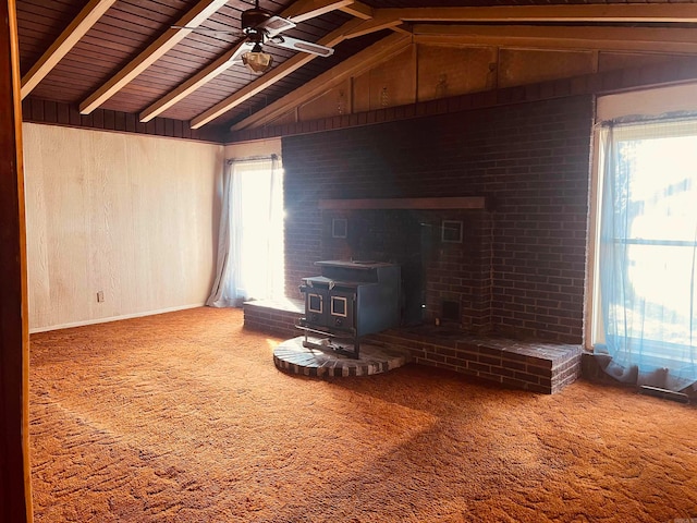 unfurnished living room featuring carpet, wood walls, a wood stove, wooden ceiling, and vaulted ceiling with beams