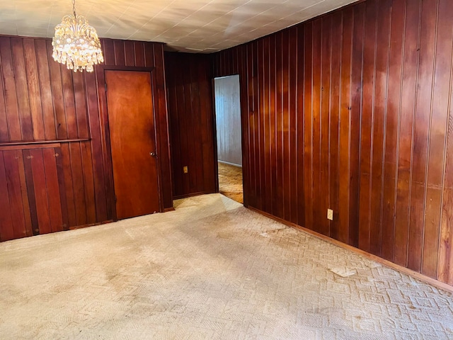 carpeted empty room featuring wood walls and a chandelier