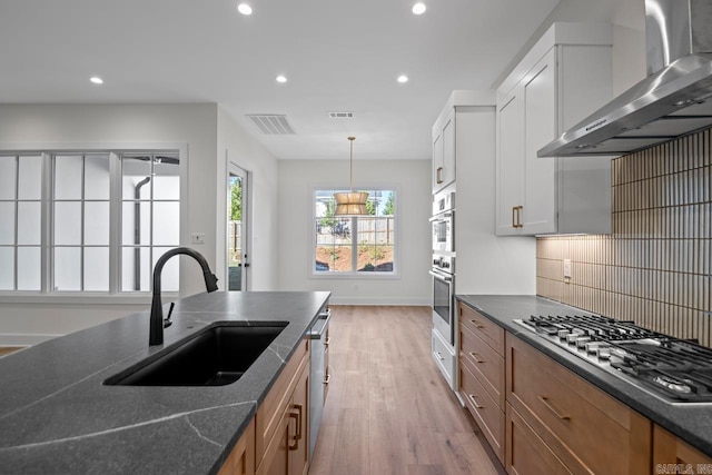 kitchen featuring wall chimney range hood, sink, light wood-type flooring, white cabinetry, and stainless steel appliances