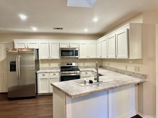 kitchen featuring sink, dark wood-type flooring, kitchen peninsula, white cabinets, and appliances with stainless steel finishes