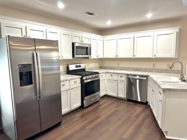 kitchen with appliances with stainless steel finishes, white cabinetry, dark wood-type flooring, and sink