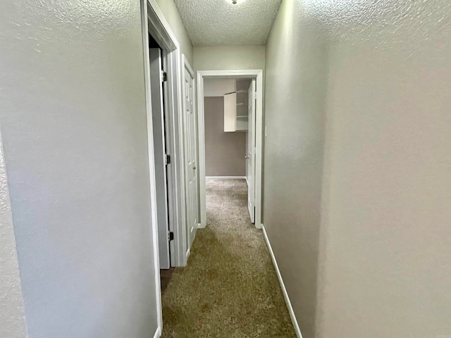 hall featuring a textured ceiling and dark carpet