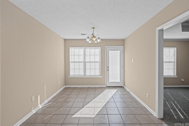 interior space featuring a healthy amount of sunlight, light tile patterned flooring, a textured ceiling, and an inviting chandelier