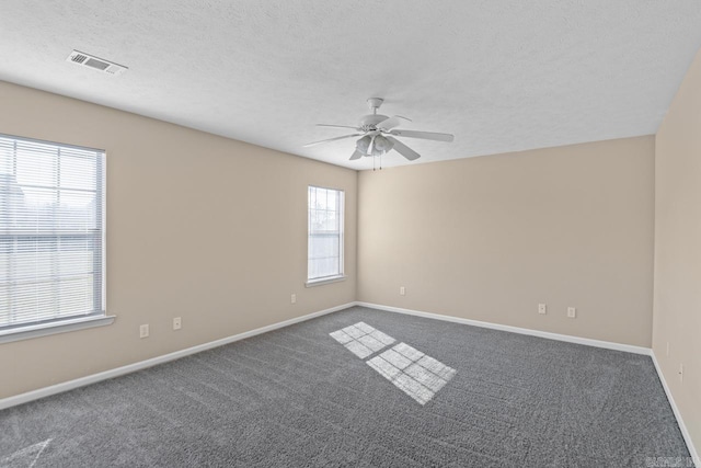 empty room with dark colored carpet, ceiling fan, and a textured ceiling