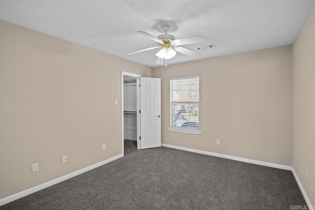 unfurnished bedroom with a textured ceiling, ceiling fan, dark colored carpet, a spacious closet, and a closet