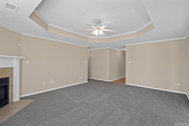 unfurnished living room with a tiled fireplace, crown molding, and a tray ceiling