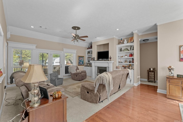 living room featuring built in shelves, ceiling fan, a textured ceiling, and light wood-type flooring