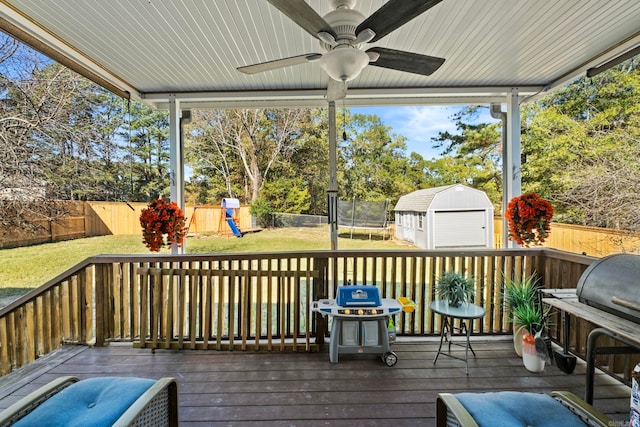 wooden deck with a trampoline, ceiling fan, a yard, a storage unit, and a playground