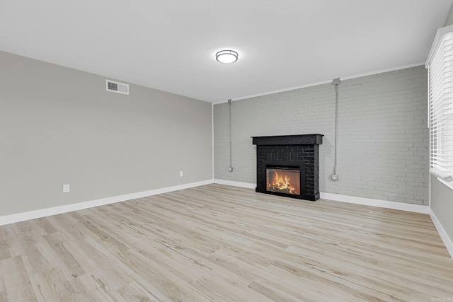 unfurnished living room with light hardwood / wood-style floors, brick wall, and a brick fireplace