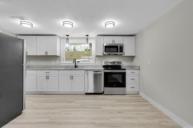 kitchen featuring pendant lighting, white cabinets, sink, light hardwood / wood-style flooring, and stainless steel appliances