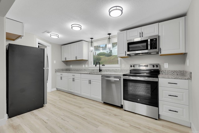 kitchen featuring white cabinets, appliances with stainless steel finishes, decorative light fixtures, and light hardwood / wood-style flooring