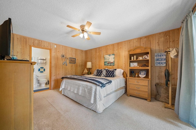 carpeted bedroom with a textured ceiling, ensuite bath, ceiling fan, and wood walls