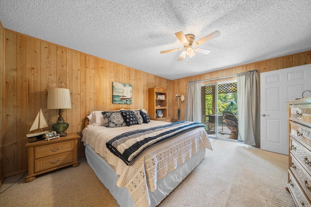 carpeted bedroom featuring a textured ceiling, access to outside, ceiling fan, and wood walls