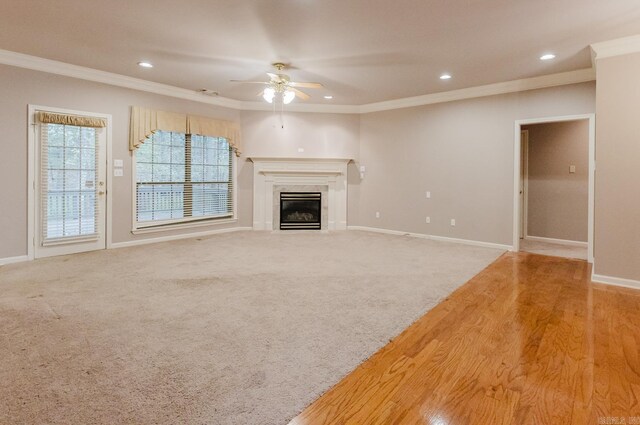 unfurnished living room featuring a premium fireplace, crown molding, ceiling fan, and light hardwood / wood-style floors