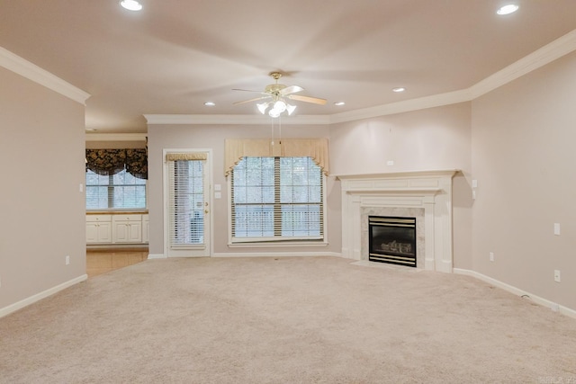 unfurnished living room with a high end fireplace, light colored carpet, ceiling fan, and crown molding