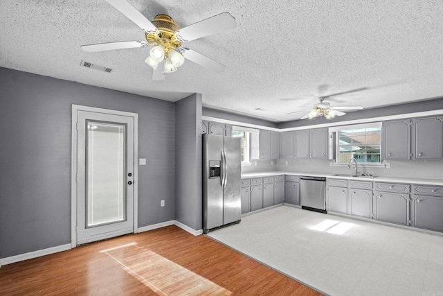 kitchen with appliances with stainless steel finishes, gray cabinetry, ceiling fan, sink, and light hardwood / wood-style floors