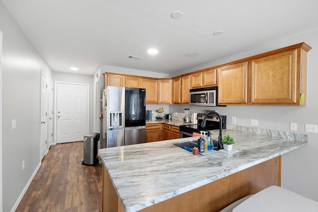 kitchen with kitchen peninsula, appliances with stainless steel finishes, dark hardwood / wood-style floors, and light stone counters