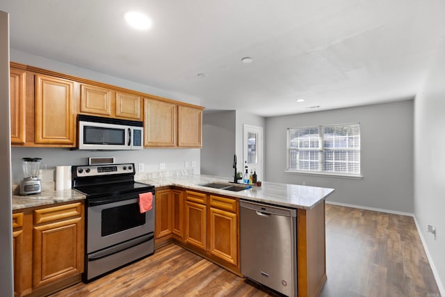 kitchen with kitchen peninsula, light stone countertops, stainless steel appliances, sink, and hardwood / wood-style flooring