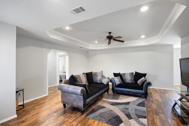 living room with a raised ceiling, crown molding, ceiling fan, and dark wood-type flooring