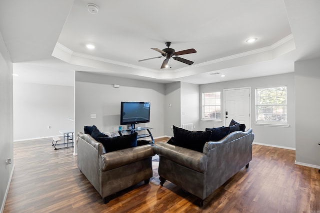 living room with ceiling fan, a raised ceiling, ornamental molding, and dark wood-type flooring