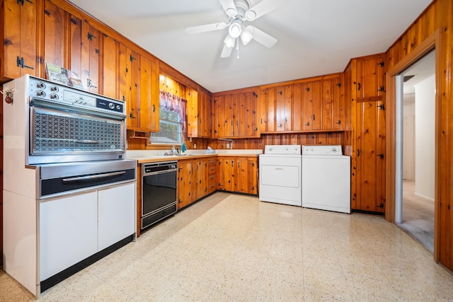 kitchen with wood walls, black appliances, sink, ceiling fan, and washing machine and clothes dryer