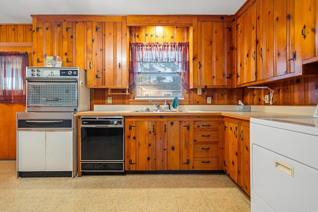 kitchen featuring dishwasher, sink, wooden walls, wall oven, and washer / clothes dryer