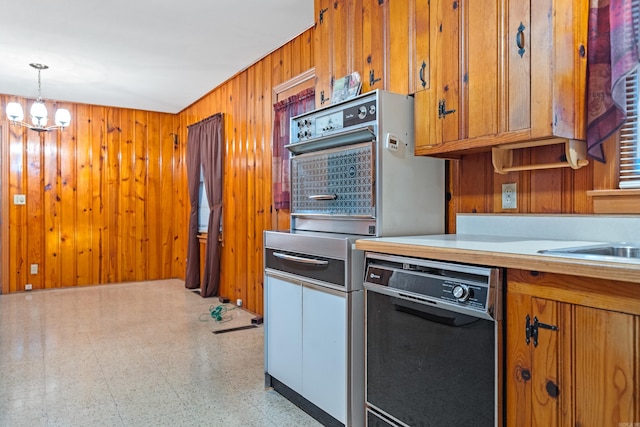 kitchen with an inviting chandelier, hanging light fixtures, wooden walls, and black appliances