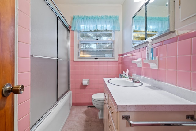 full bathroom featuring vanity, toilet, bath / shower combo with glass door, and tile walls