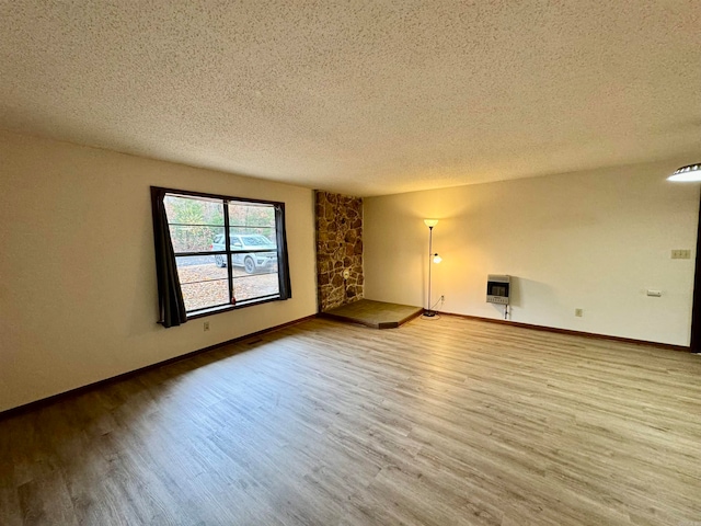 empty room with a textured ceiling, hardwood / wood-style flooring, and heating unit