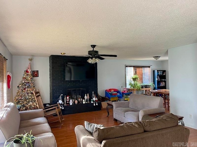 living room with ceiling fan, a fireplace, wood-type flooring, and a textured ceiling