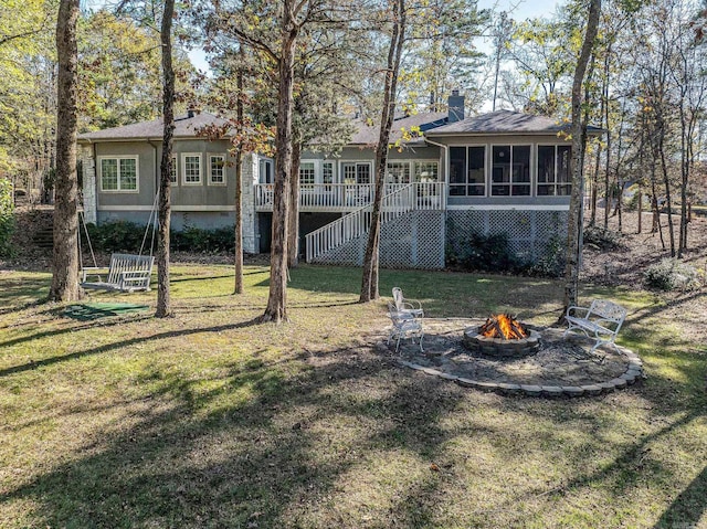 rear view of property with a lawn, a wooden deck, a sunroom, and an outdoor fire pit