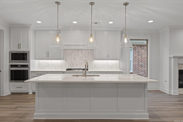 kitchen featuring a center island with sink, white cabinets, decorative light fixtures, and appliances with stainless steel finishes